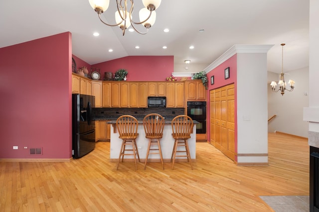 kitchen with a center island, lofted ceiling, black appliances, a kitchen breakfast bar, and a notable chandelier