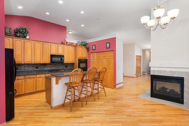 kitchen with decorative backsplash, a breakfast bar, a kitchen island, black appliances, and light wood-type flooring