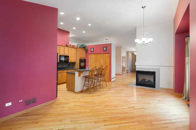 kitchen featuring decorative light fixtures, a breakfast bar area, a fireplace, black appliances, and light wood-type flooring