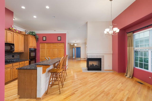 kitchen featuring backsplash, black appliances, a center island with sink, a fireplace, and light hardwood / wood-style floors