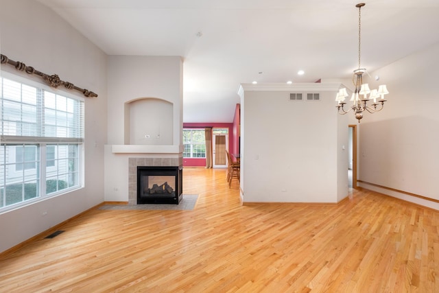 unfurnished living room featuring light wood-type flooring, a notable chandelier, and a tiled fireplace