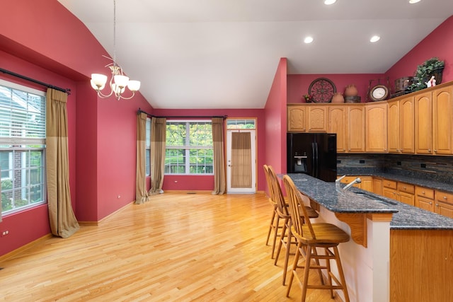 kitchen featuring decorative backsplash, vaulted ceiling, black refrigerator with ice dispenser, and light hardwood / wood-style flooring