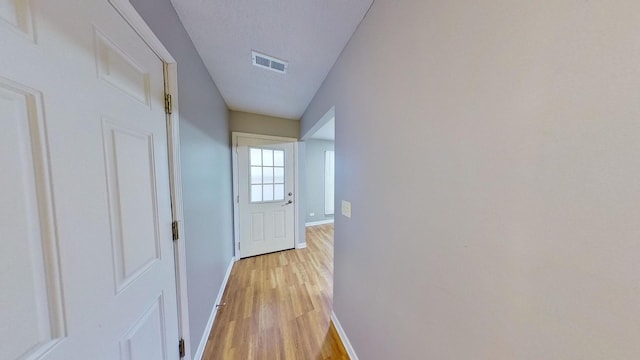 corridor with light wood-type flooring and a textured ceiling