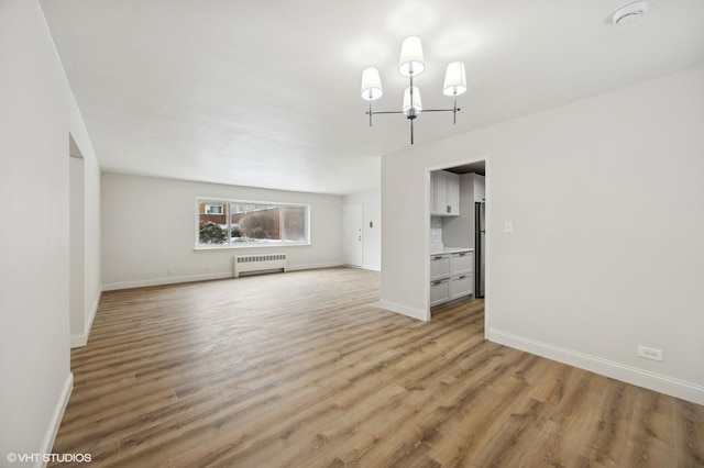 unfurnished living room with an inviting chandelier, radiator heating unit, baseboards, and light wood-type flooring