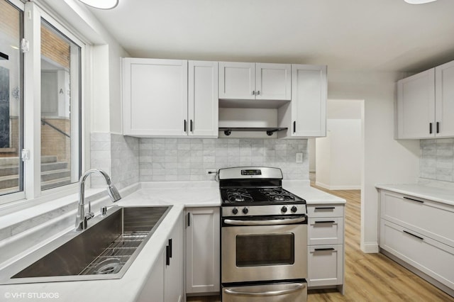 kitchen featuring a sink, stainless steel range with gas stovetop, decorative backsplash, light wood-style flooring, and open shelves