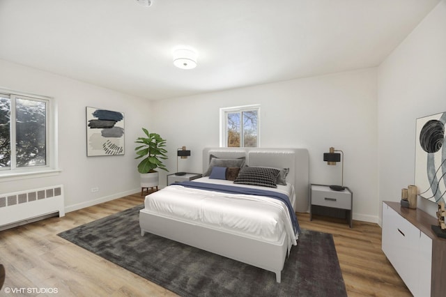 bedroom featuring baseboards, multiple windows, wood finished floors, and radiator heating unit