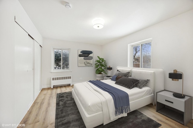 bedroom with a closet, multiple windows, radiator, and light wood finished floors