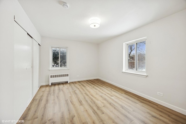 unfurnished bedroom with a closet, multiple windows, radiator, and light wood-type flooring