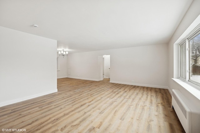 empty room featuring baseboards, a notable chandelier, radiator heating unit, and light wood finished floors