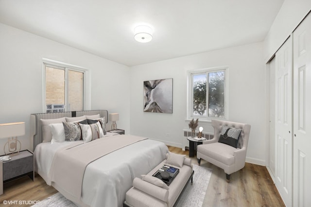 bedroom featuring light wood-type flooring, a closet, baseboards, and radiator