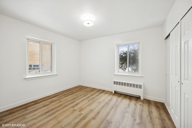 unfurnished bedroom with radiator heating unit, wood finished floors, a closet, and baseboards