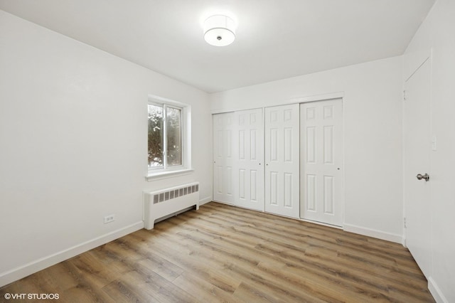 unfurnished bedroom with a closet, radiator, baseboards, and wood finished floors