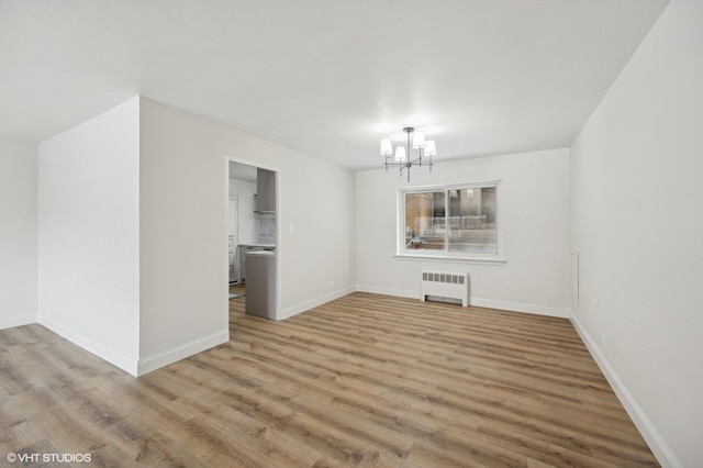 spare room with a chandelier, light wood-style flooring, radiator heating unit, and baseboards