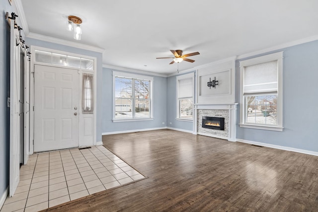 entrance foyer featuring ceiling fan, ornamental molding, a barn door, and a stone fireplace