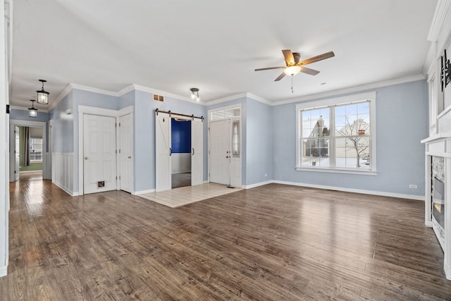 unfurnished living room featuring crown molding, a premium fireplace, dark hardwood / wood-style floors, and a barn door