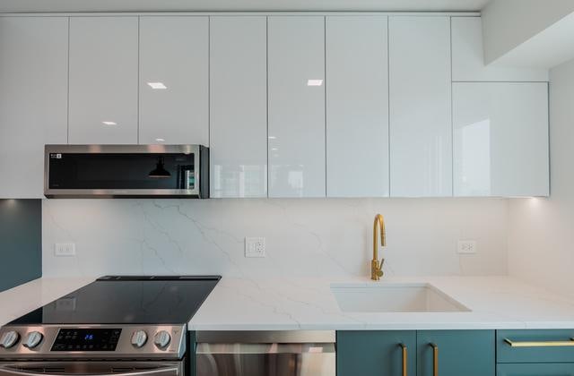 kitchen featuring tasteful backsplash, light stone counters, sink, white cabinets, and range