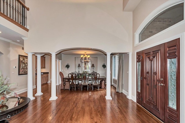 entryway with arched walkways, a high ceiling, ornamental molding, dark wood-style floors, and decorative columns