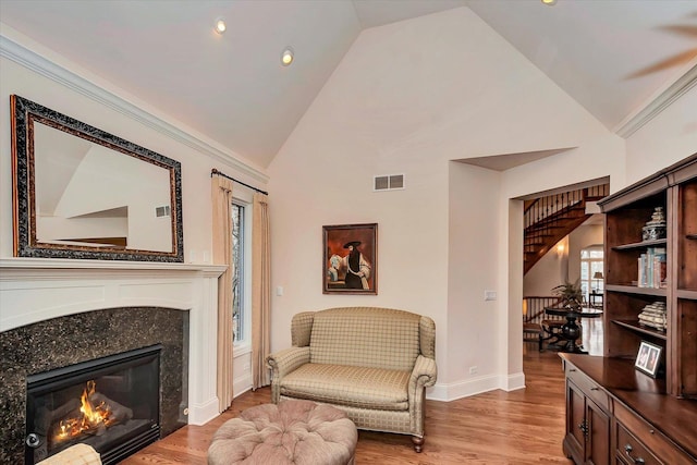 living area featuring light wood-type flooring, a high end fireplace, visible vents, and baseboards