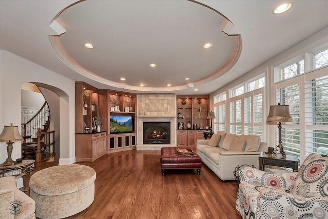 living area with a tiled fireplace, stairway, a raised ceiling, and wood finished floors