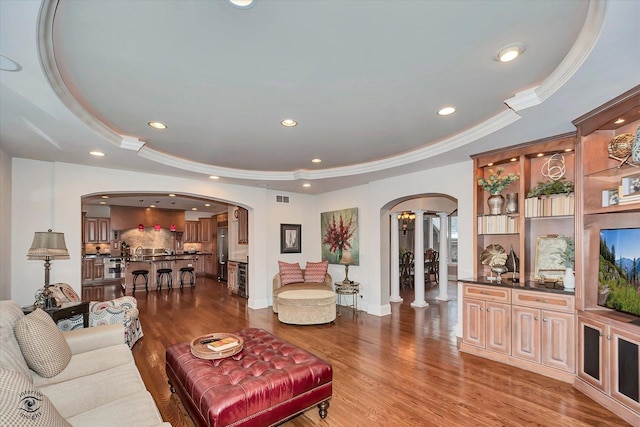 living room with arched walkways, light wood-type flooring, a raised ceiling, and crown molding