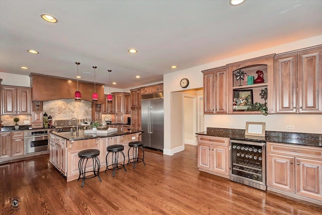 kitchen with wine cooler, a kitchen breakfast bar, appliances with stainless steel finishes, a center island with sink, and pendant lighting