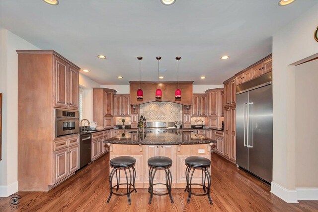 kitchen with an island with sink, appliances with stainless steel finishes, a kitchen breakfast bar, dark stone countertops, and decorative light fixtures