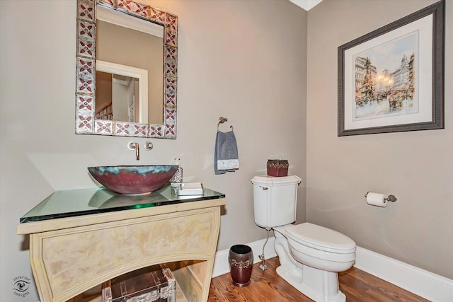 half bath featuring wood finished floors, toilet, and baseboards