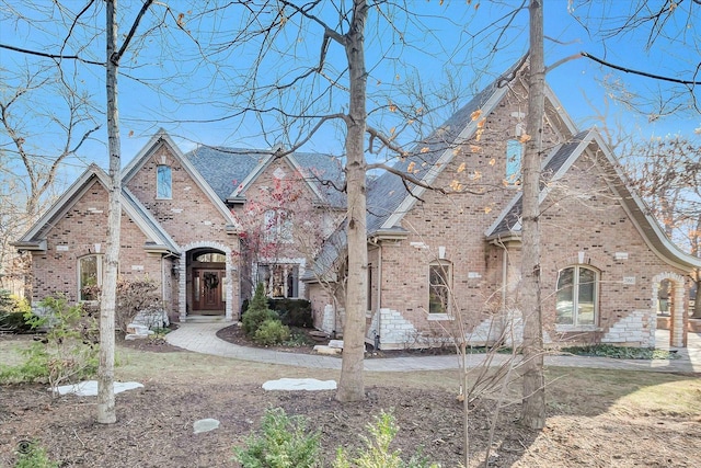 tudor home featuring brick siding and roof with shingles