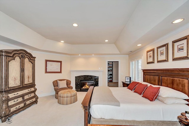 bedroom with a tray ceiling, crown molding, a premium fireplace, light carpet, and baseboards