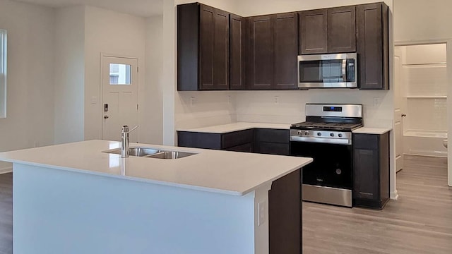 kitchen featuring sink, stainless steel appliances, light hardwood / wood-style floors, and a center island with sink