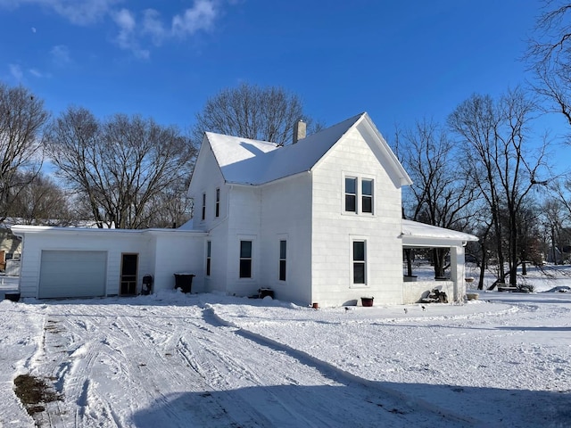 snow covered property with a garage and a chimney