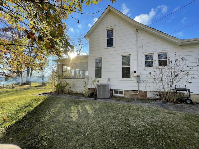 back of property with central air condition unit, a sunroom, and a lawn