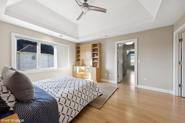 bedroom with ceiling fan, a raised ceiling, and light wood-type flooring