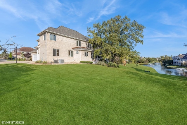 rear view of house with a lawn, a water view, cooling unit, and a garage