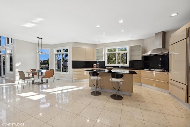 kitchen with stainless steel gas stovetop, a center island, backsplash, wall chimney range hood, and sink