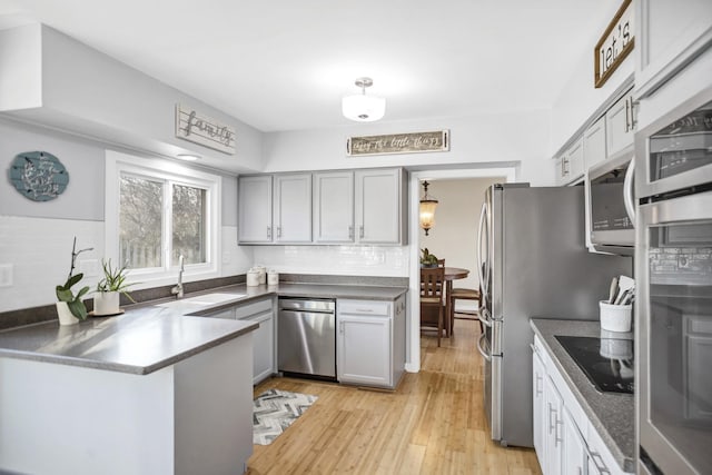 kitchen with backsplash, light wood-style flooring, appliances with stainless steel finishes, a sink, and a peninsula