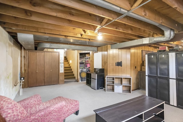 finished basement with wood walls, stairs, carpet flooring, and freestanding refrigerator