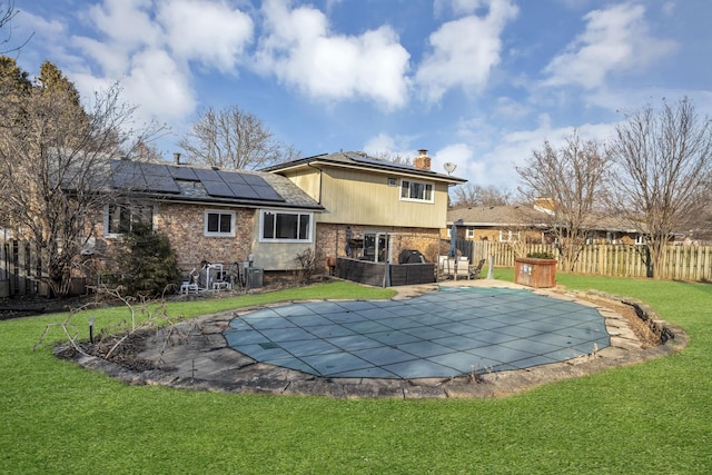 back of property with a fenced in pool, a patio, a chimney, a lawn, and roof mounted solar panels