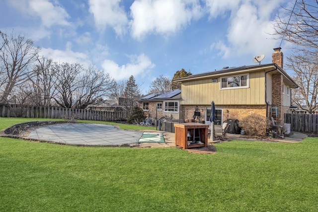 back of house with brick siding, a yard, roof mounted solar panels, a chimney, and a patio area