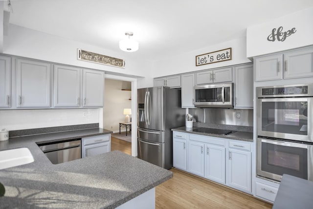 kitchen featuring stainless steel appliances, light wood-type flooring, dark countertops, and gray cabinets