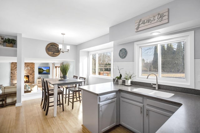 kitchen featuring a peninsula, gray cabinets, light wood-style floors, a fireplace, and a sink