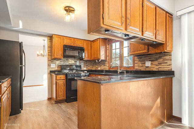 kitchen featuring pendant lighting, sink, light hardwood / wood-style floors, black appliances, and kitchen peninsula