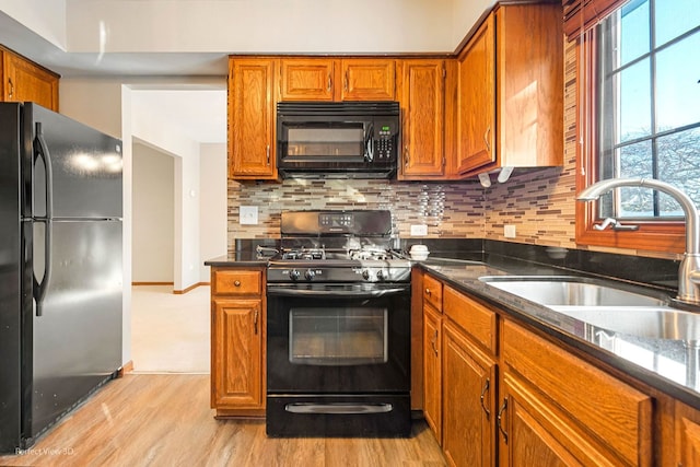 kitchen with sink, dark stone countertops, decorative backsplash, light hardwood / wood-style floors, and black appliances