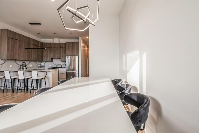 kitchen with a breakfast bar area, light wood-style flooring, decorative backsplash, freestanding refrigerator, and modern cabinets