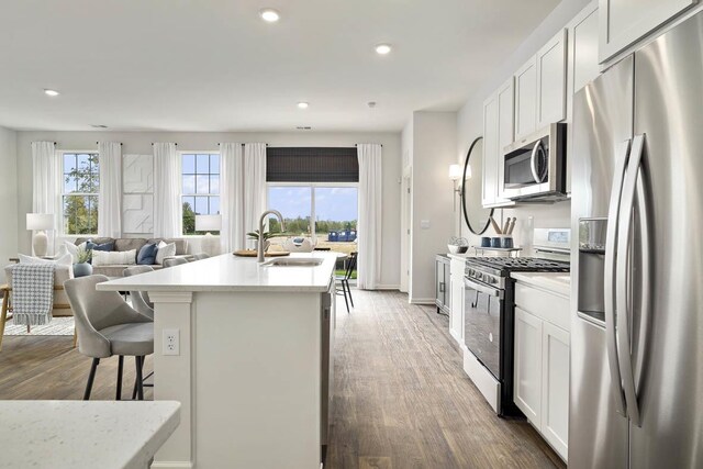 kitchen with sink, hardwood / wood-style flooring, appliances with stainless steel finishes, a kitchen island with sink, and white cabinets