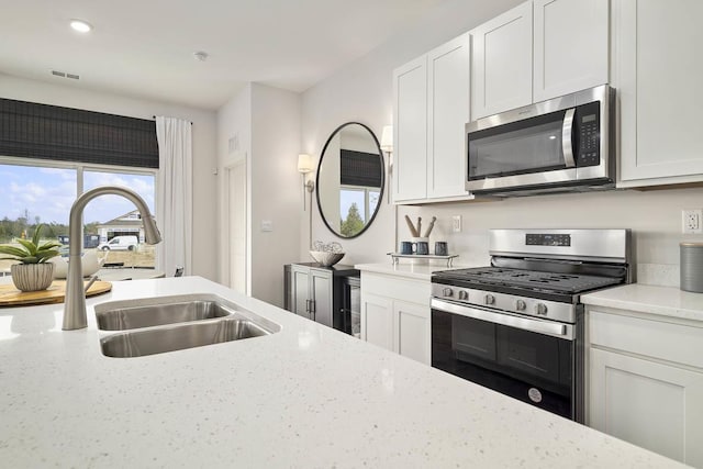 kitchen with light stone countertops, appliances with stainless steel finishes, sink, and white cabinets