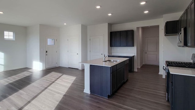 kitchen with dark wood-type flooring, stainless steel appliances, sink, and a kitchen island with sink