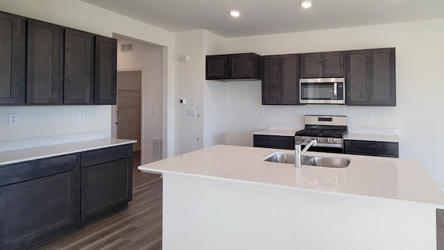 kitchen featuring sink, appliances with stainless steel finishes, a kitchen island with sink, light stone countertops, and dark hardwood / wood-style flooring