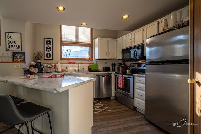 kitchen with a breakfast bar, kitchen peninsula, sink, white cabinetry, and appliances with stainless steel finishes