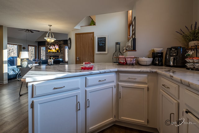 kitchen featuring lofted ceiling, white cabinetry, a stone fireplace, dark hardwood / wood-style floors, and ceiling fan